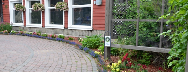 Flower bed and hanging plants along a red building with white windows