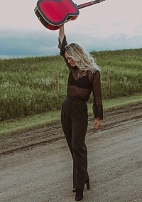 Jimi on a dirt road, holing her acoustic guitar aloft.