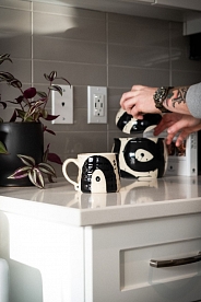 White and black pottery on a kitchen counter. A hand is opening a vessel with a lid.