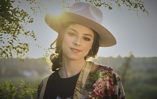 Headshot of Hailey Benedict in a wide-brimmed hat with the sun behind her.