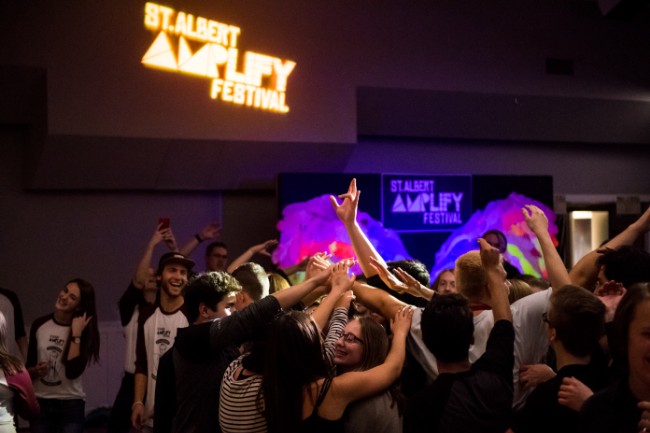 Youth in a crowd, dancing and rising their hands in the air.