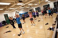 Photo of a fitness class lifting weights above their heads