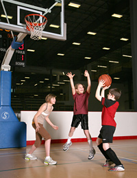 Photo of a boy taking a shot at a basketball net with a girl and boy trying to block the shot