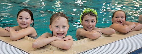A photo of four kids in the pool leaning against the edge smiling