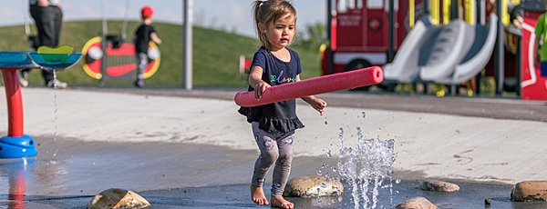 A child plays with a pool noodle at the splash park.