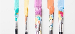 Paint brushes lined up with different colours on the tips