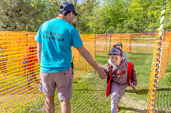 A volunteer wearing a blue shirt high fiving a child running through a maze