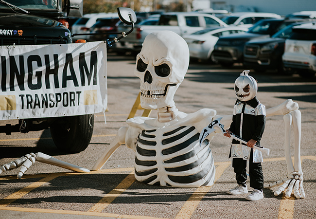 Child in Halloween costume standing beside giant skeleton