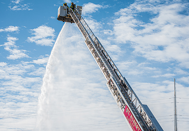 Aerial Fire Truck arm reaching into the sky with firefighters spraying water