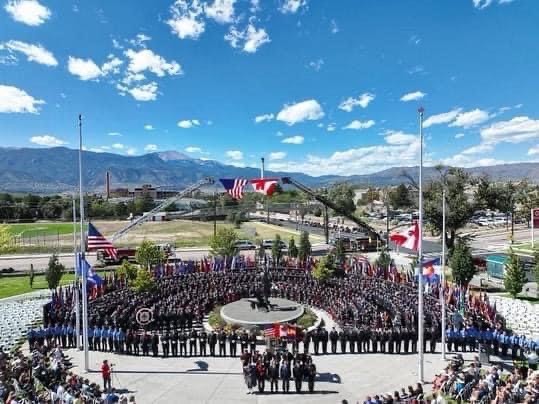 Image of many firefighters standing in front of two fire trucks with a Canadian and American flag raised.