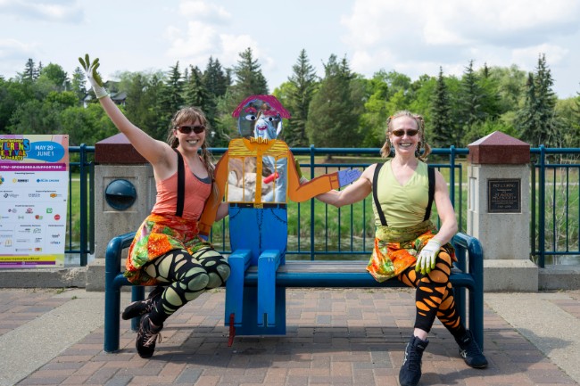two roving performers pose with an art installation on a bench