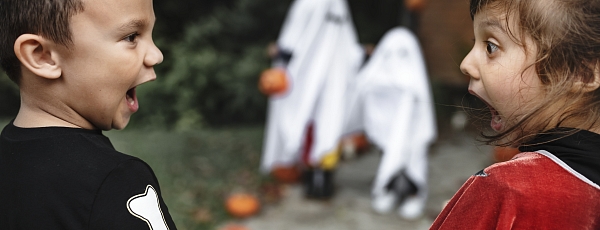Two children in Halloween costumes are scared by two ghosts in the background.